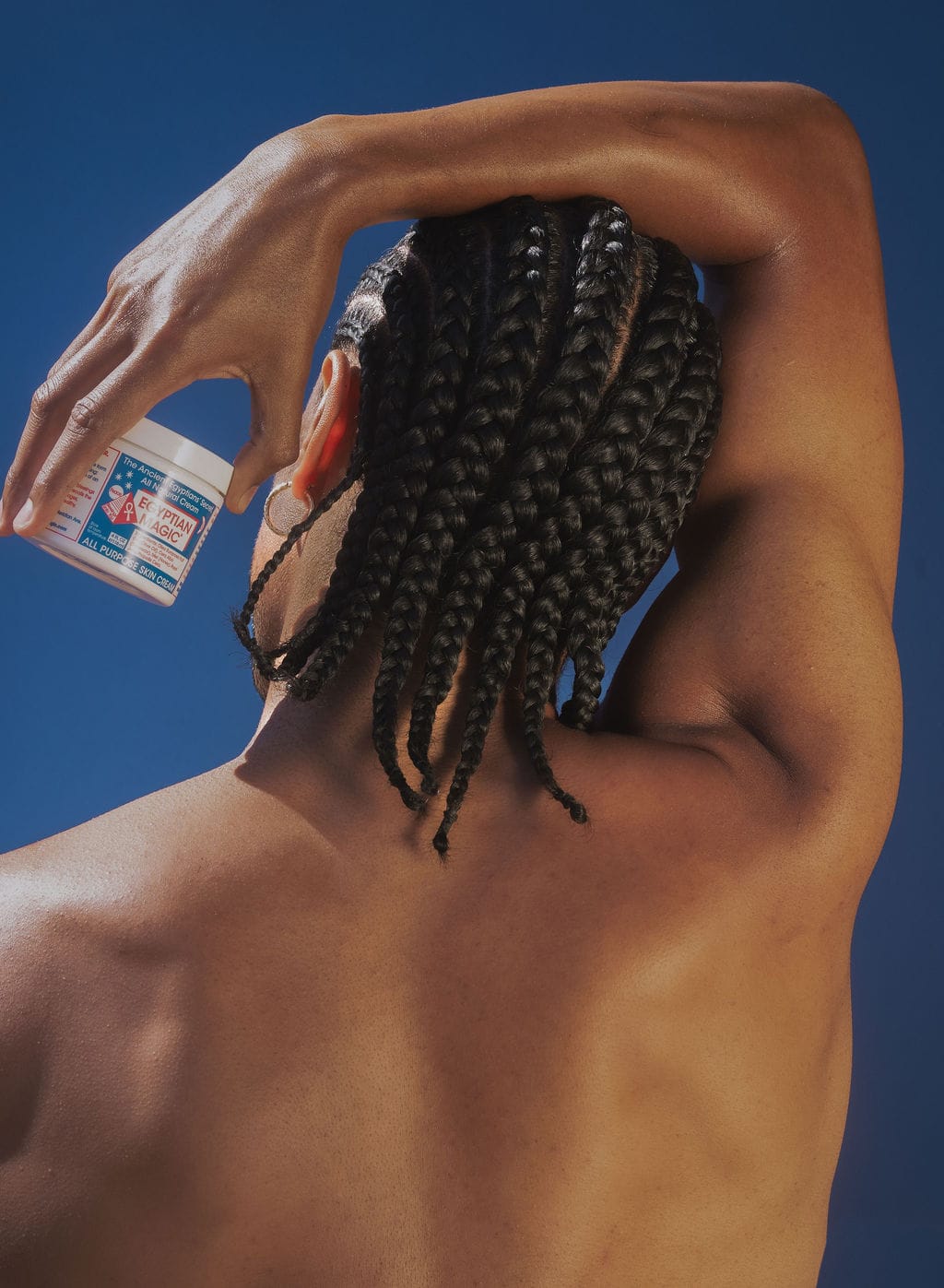 Model with long braids holding a jar of Egyptian Magic beside his ear