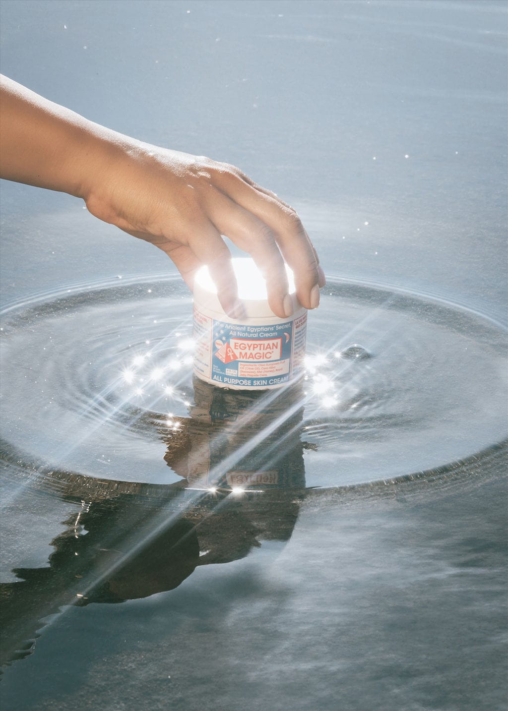 A hand pressing a jar of Egyptian Magic into rippling water